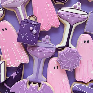 Puede incluir: Galletas de az&uacute;car de Halloween de color morado y rosa decoradas con glaseado. Las galletas tienen forma de fantasmas, murci&eacute;lagos, telara&ntilde;as, sombreros de bruja, copas de champ&aacute;n y bolsas de la compra.