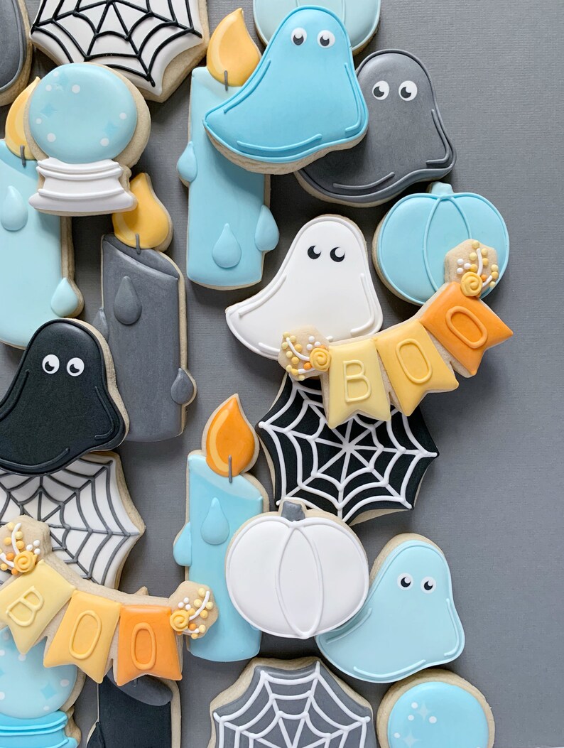 May include: A collection of Halloween-themed sugar cookies decorated with various designs, including ghosts, pumpkins, candles, and spiderwebs. The cookies are decorated in shades of blue, white, orange, and gray.