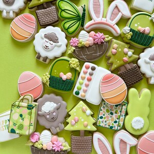 May include: A collection of Easter-themed sugar cookies decorated with various designs, including bunnies, lambs, baskets, eggs, and trees. The cookies are on a green background.