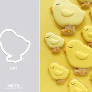Op de afbeelding: Een set koekjesvormen in de vorm van kuikens. De vormen zijn gemaakt van metaal en hebben een witte afwerking. De vormen zijn in een rij op een witte achtergrond gerangschikt. Het woord "CHICK" is onder de vormen gedrukt.