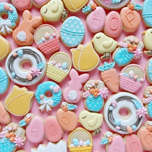 May include: A collection of Easter-themed sugar cookies decorated with various designs, including bunnies, chicks, baskets, eggs, and wreaths. The cookies are decorated with pastel colors, including pink, blue, yellow, and green.