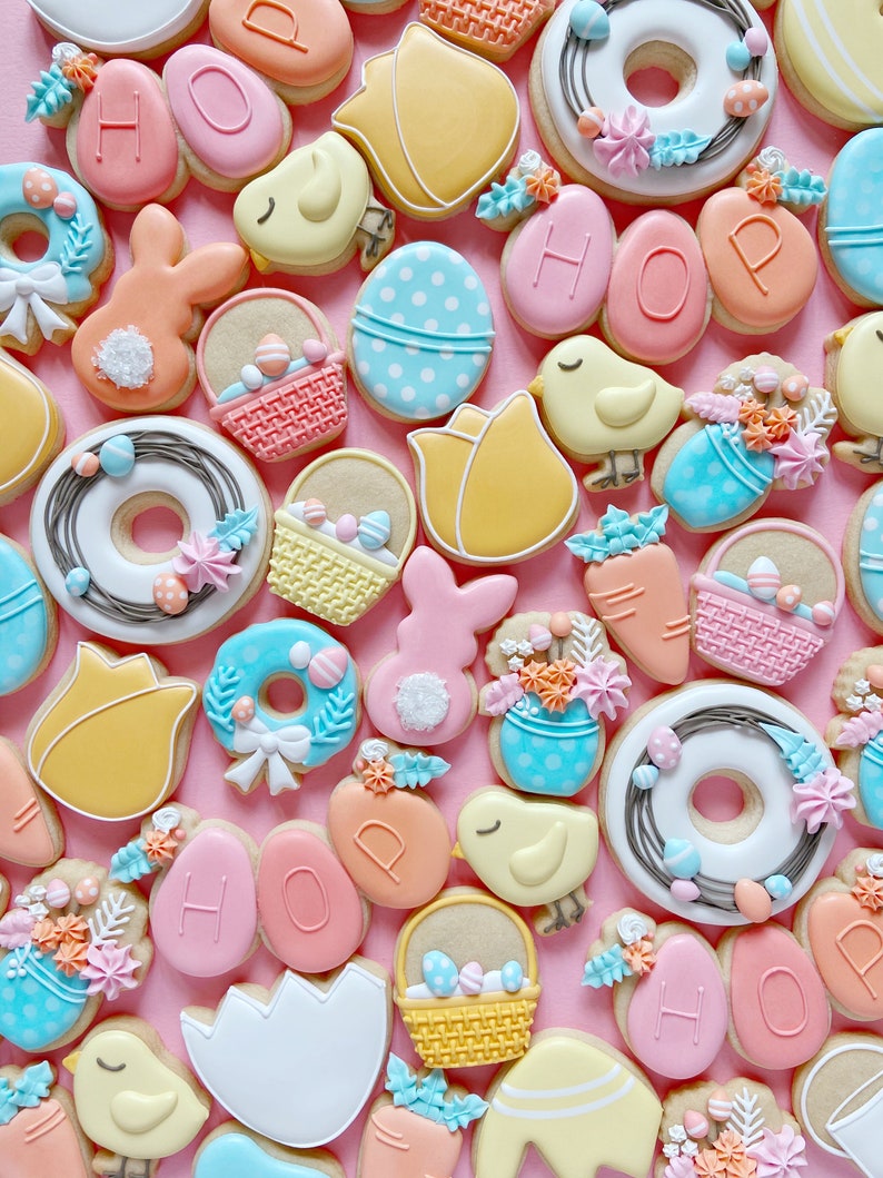 May include: A collection of Easter-themed sugar cookies decorated with various designs, including bunnies, chicks, baskets, eggs, and wreaths. The cookies are decorated with pastel colors, including pink, blue, yellow, and green.