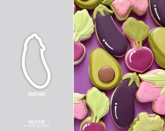 May include: A set of cookie cutters featuring various vegetables, including eggplant, avocado, radish, and a leafy green vegetable. The cutters are made of white plastic and are arranged on a light gray background. The text "EGGPLANT" and "HOLLY FOX COOKIE CUTTERS" is printed below the cutters.