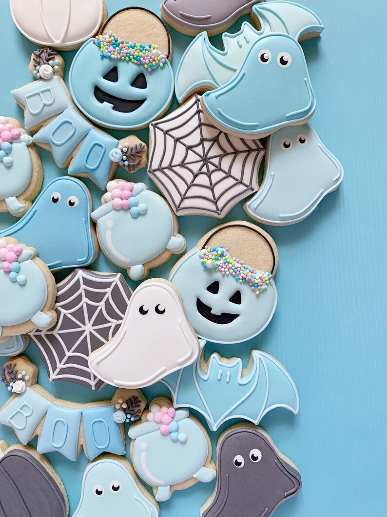May include: A collection of Halloween-themed sugar cookies decorated with blue, white, and gray icing. The cookies feature ghosts, bats, pumpkins, spiderwebs, and a "BOO" banner.