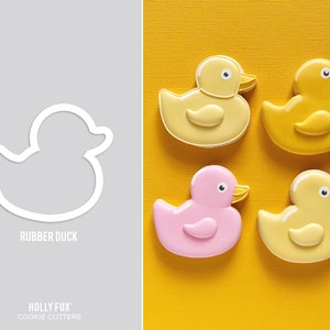 May include: Four cookie cutters shaped like rubber ducks. Two are yellow, one is pink, and one is a white outline. The cookie cutters are on a yellow background. The text "Rubber Duck" is below the white outline cookie cutter. The text "Holly Fox Cookie Cutters" is at the bottom of the image.