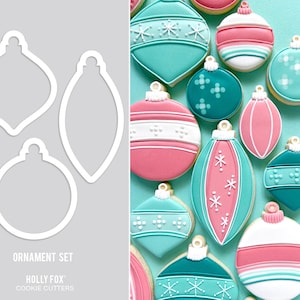 May include: A set of three cookie cutters shaped like Christmas ornaments. The cutters are made of white metal and are shown against a gray background. The cutters are labeled "Ornament Set" and "Holly Fox Cookie Cutters".