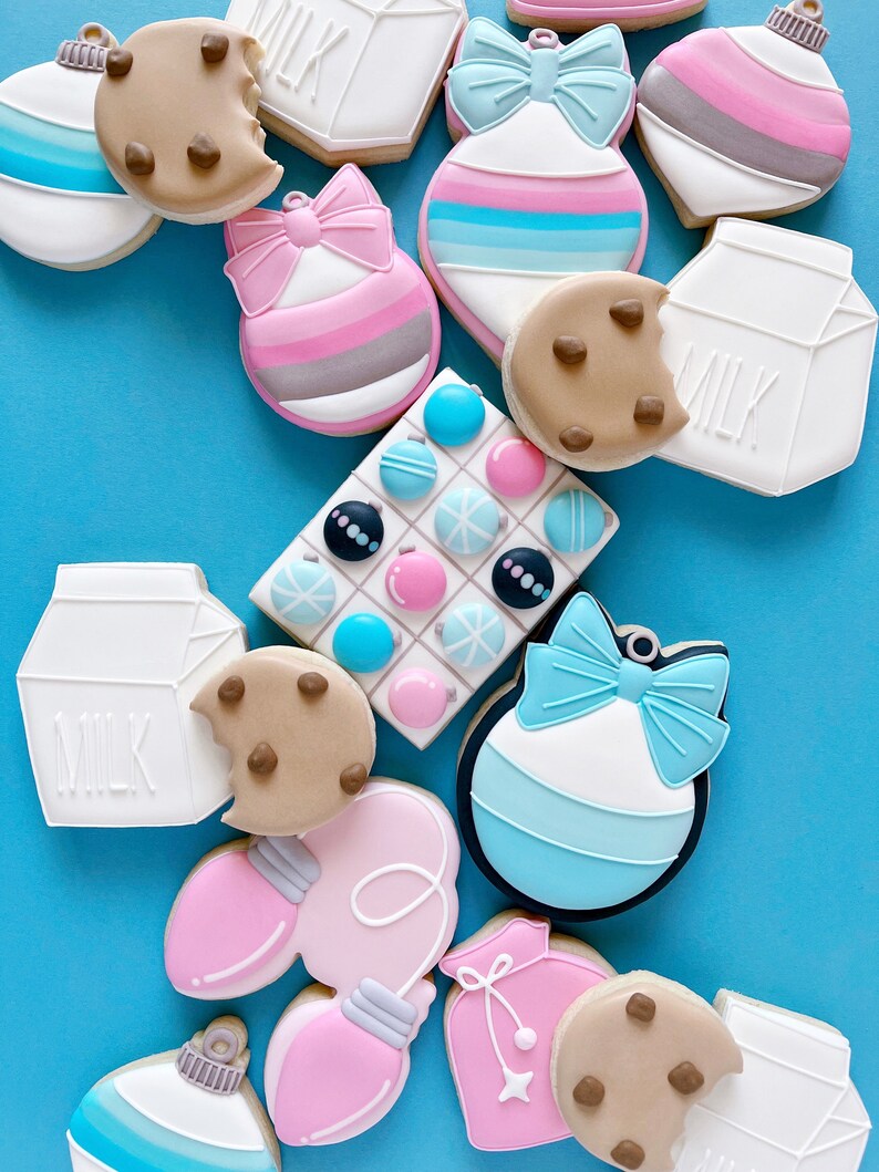 May include: Assortment of Christmas-themed sugar cookies decorated with various colors and designs, including ornaments, milk cartons, and a cookie with chocolate chips.
