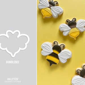 May include: A set of four cookie cutters shaped like bumblebees. The cutters are made of white plastic and are shown against a gray background. The word "Bumblebee" is printed below the cutters. The words "Holly Fox" and "Cookie Cutters" are printed below the word "Bumblebee".