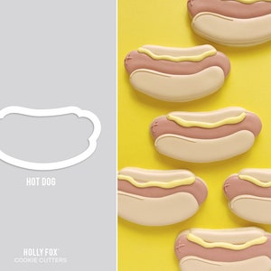 May include: A set of six cookie cutters shaped like hot dogs. The cutters are white and are arranged in a row on a light gray background. The text "HOT DOG" is printed below the cutters. The text "HOLLY FOX: COOKIE CUTTERS" is printed below the text "HOT DOG".