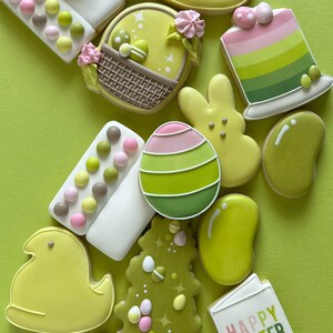 May include: A collection of Easter-themed sugar cookies decorated with pastel colors and various designs, including chicks, bunnies, eggs, a basket, a tree, and a sign that says "Happy Easter".