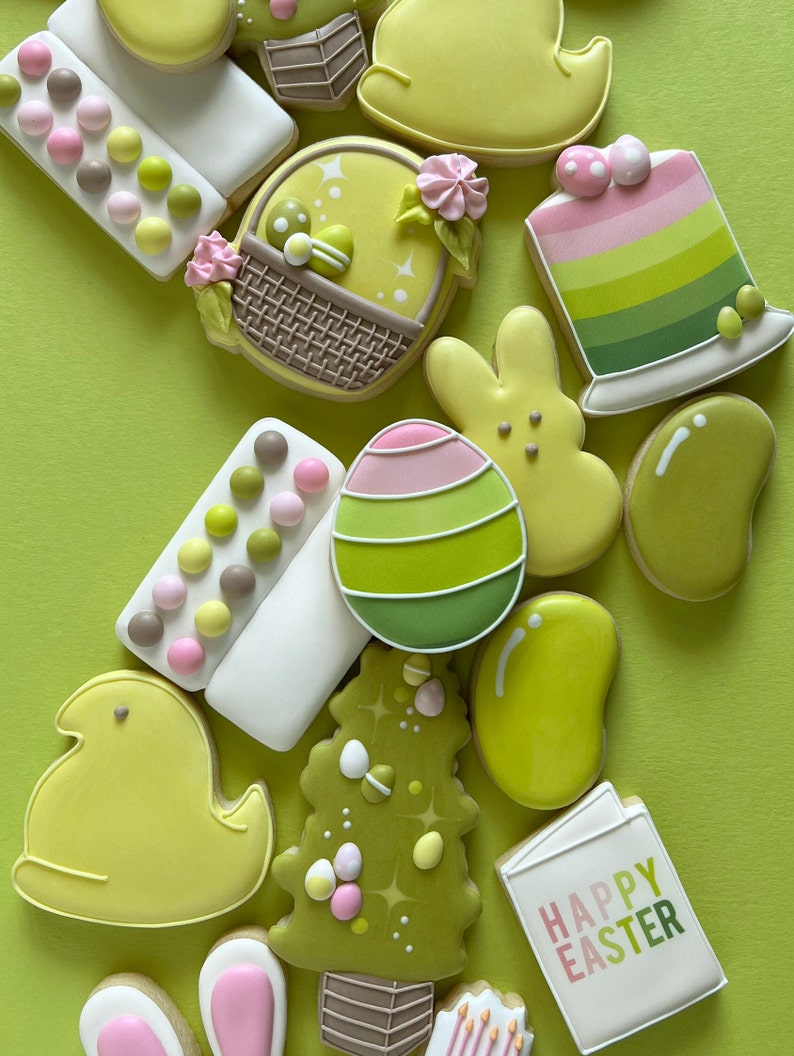 May include: A collection of Easter-themed sugar cookies decorated with pastel colors and various designs, including chicks, bunnies, eggs, a basket, a tree, and a sign that says "Happy Easter".