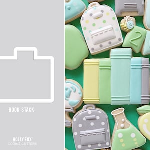 May include: A set of cookie cutters for making back-to-school themed cookies. The cutters include a stack of books, a backpack, a beaker, and an apple. The cutters are made of metal and have a white finish.
