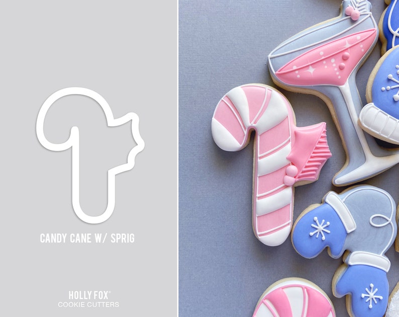 Pode incluir: Um cortador de biscoitos branco em forma de bengala de caramelo com um ramo de azevinho. O cortador est&aacute; sobre um fundo cinza. O texto "CANDY CANE W/ SPRIG" est&aacute; abaixo do cortador. O texto "HOLLY FOX" e "COOKIE CUTTERS" est&aacute; abaixo do texto.