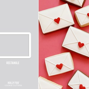 May include: A set of six white cookie cutters shaped like envelopes with red hearts on the front. The cookie cutters are on a pink background. The text "RECTANGLE" is printed below the cookie cutters. The text "HOLLY FOX COOKIE CUTTERS" is printed below the text "RECTANGLE".