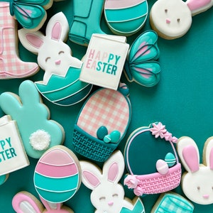 May include: A collection of Easter-themed sugar cookies decorated with pastel pink, blue, and green icing. The cookies feature bunnies, eggs, butterflies, baskets, and a sign that reads "Happy Easter".