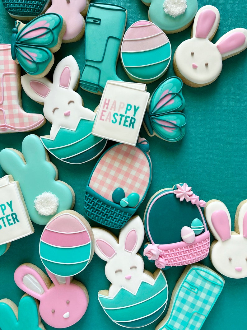 May include: A collection of Easter-themed sugar cookies decorated with pastel pink, blue, and green icing. The cookies feature bunnies, eggs, butterflies, baskets, and a sign that reads "Happy Easter".