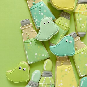 May include: A collection of decorated sugar cookies in the shape of ghosts and potion bottles. The cookies are decorated with green, yellow, and white icing and have a whimsical, spooky theme.