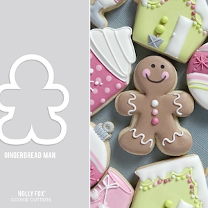 May include: A gingerbread man cookie cutter, shown with a variety of other cookie cutters, including a gingerbread house, a Christmas ornament, and a cupcake. The cookie cutters are all white and have a smooth finish. The gingerbread man cookie cutter is shaped like a traditional gingerbread man, with a round head, arms, and legs. The cookie cutter is labeled "Gingerbread Man" and "Holly Fox Cookie Cutters".