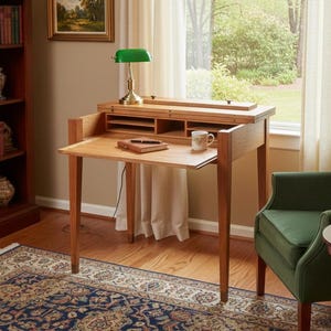 May include: A wooden writing desk with a pull-out writing surface and storage compartments. A green desk lamp sits on top. A green armchair is to the right of the desk. A rug with a blue and gold pattern is on the floor.