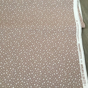 May include: A beige fabric with a white polka dot and star pattern. The fabric is labeled "Design #19680 for ELIZABETH HARTMAN for ROBERT KAUFMAN...roberkaufman.com."