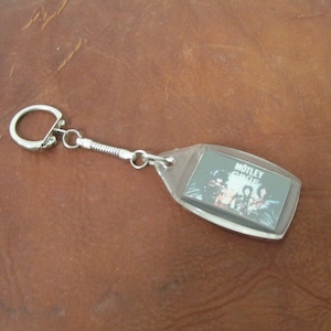 May include: A silver keyring with a spring-loaded chain and a clear plastic charm featuring a black and white image of the band Motley Crue.