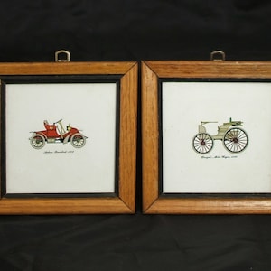 May include: Two framed vintage illustrations of antique cars. The left frame shows a red car with the text "Stutz Bearcat 1912". The right frame shows a white car with the text "Duryea Motor Wagon 1900".