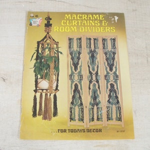 May include: A vintage book cover with the title "Macrame Curtains & Room Dividers" in gold lettering. The cover features a macrame plant hanger with a potted plant and a macrame room divider. The background is a golden yellow.