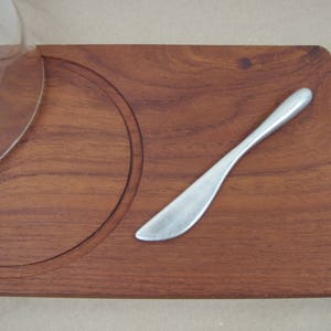 May include: A wooden cheese board with a circular groove and a silver butter knife.