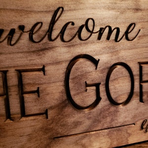 May include: A wooden sign with the words "Welcome to the Golf" carved into it. The sign has a rustic brown finish.