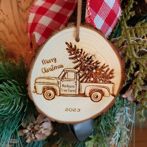 May include: A wooden Christmas ornament with a burnt-in design of a vintage pickup truck carrying a Christmas tree. The ornament is decorated with the text "Merry Christmas", "Markiano Tree Farm", and "2023".