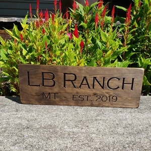 May include: A dark brown wooden sign with the text "LB Ranch MT. EST. 2019" carved into it.