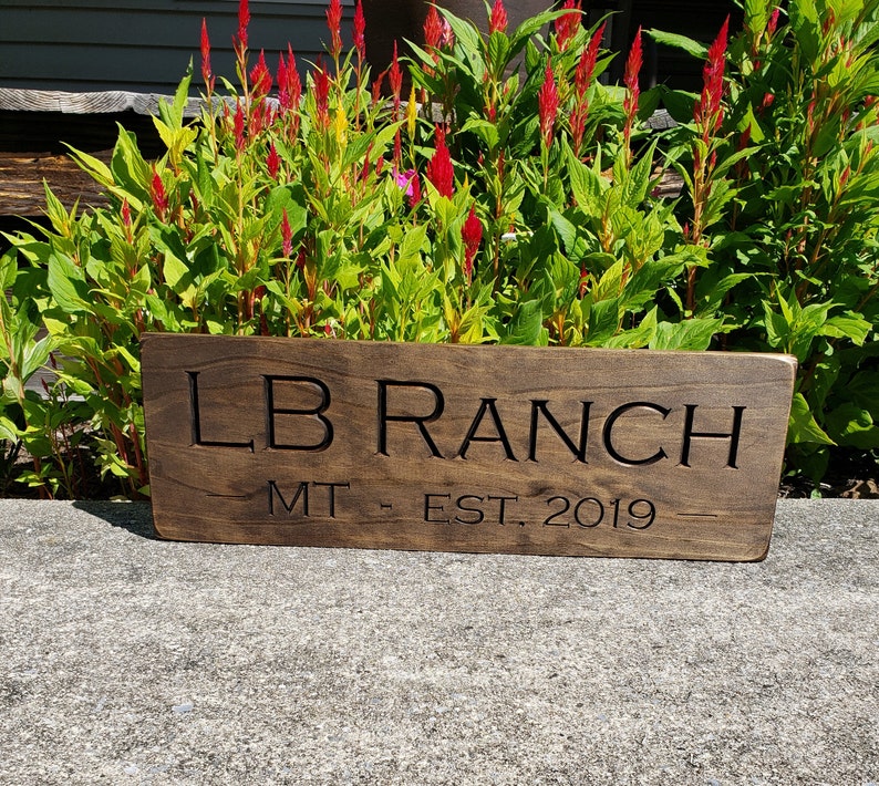 May include: A dark brown wooden sign with the text "LB Ranch MT. EST. 2019" carved into it.