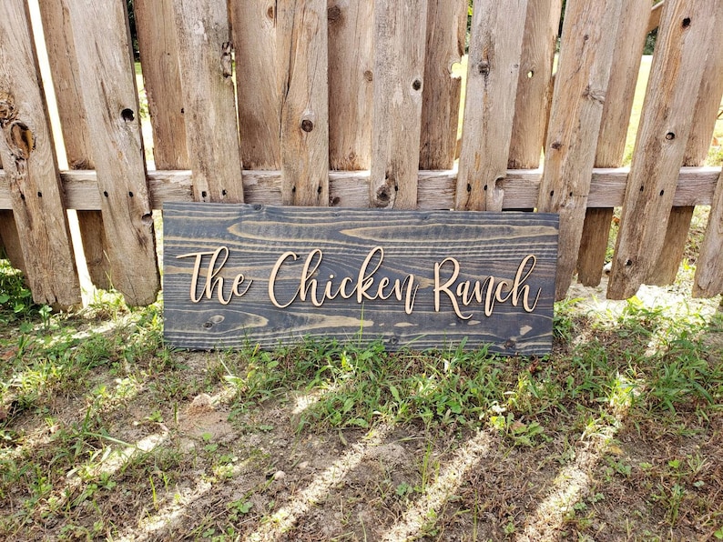 May include: A rustic wooden sign with the text "The Chicken Ranch" in a cursive font.