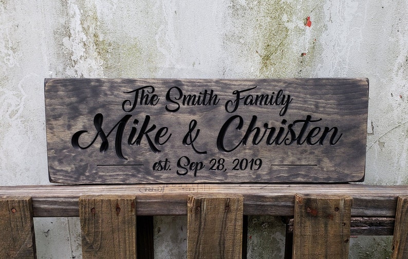 May include: A dark brown wooden sign with the text "The Smith Family Mike & Christen est. Sep 28, 2019" carved into it.