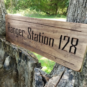May include: A wooden sign with the text "Ranger Station 128" carved into it. The sign is brown and has a rustic look.
