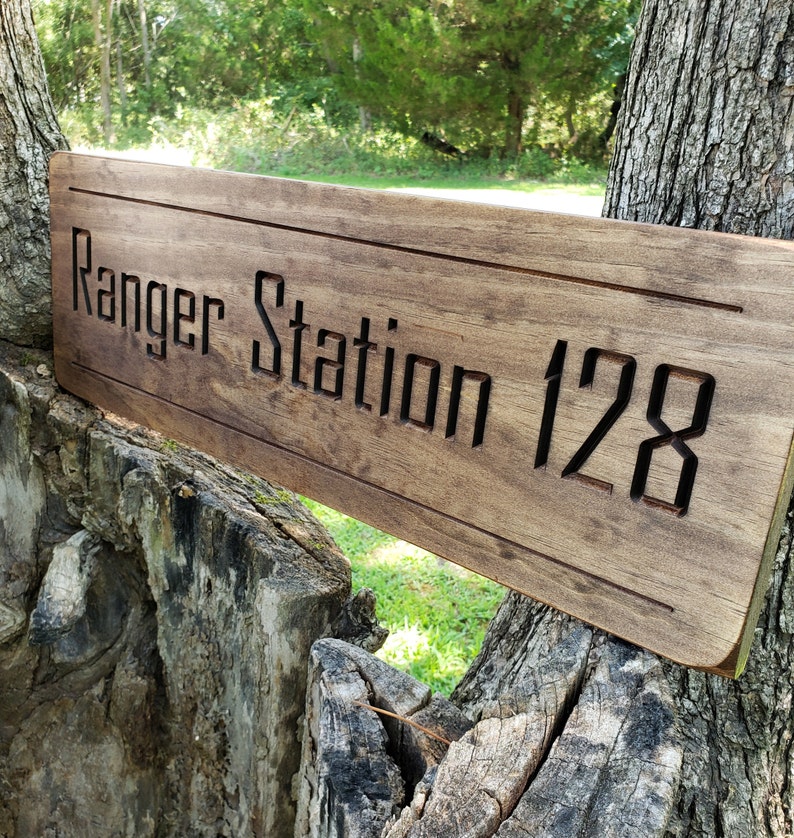 May include: A wooden sign with the text "Ranger Station 128" carved into it. The sign is brown and has a rustic look.