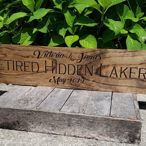 May include: A wooden sign with the text "Victoria & James Retired Hidden Lakers May 2019" engraved on it.