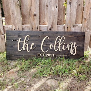 May include: A dark wood sign with the text "The Collins EST 2021" in a light wood font.