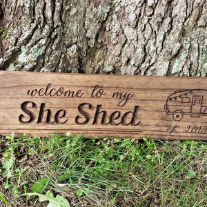 May include: A wooden sign with the text "welcome to my She Shed est. 2019" and a small illustration of a camper.
