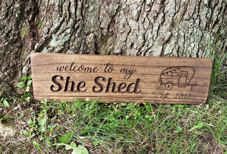 May include: A wooden sign with the text "welcome to my She Shed est. 2019" and a small illustration of a camper.