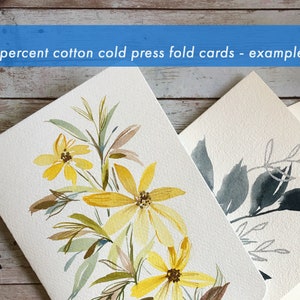 Peut inclure: Cartes de v&oelig;ux florales &agrave; l'aquarelle. Une carte pr&eacute;sente des fleurs jaunes avec des feuilles marron et vertes. Une autre carte a un motif de feuilles grises et argent&eacute;es. Les cartes sont en papier blanc textur&eacute;. Le texte en haut indique "100 percent cotton cold press fold cards - example only."
