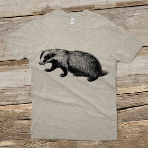 Puede incluir: Una camiseta gris jaspeada con una ilustraci&oacute;n en blanco y negro de un tej&oacute;n.