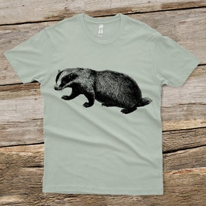 Puede incluir: Una camiseta verde claro con una ilustraci&oacute;n en blanco y negro de un tej&oacute;n.
