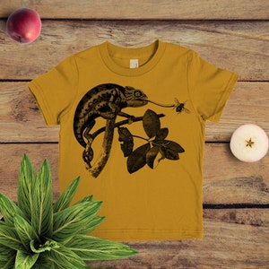 May include: A mustard yellow t-shirt featuring a black and white illustration of a chameleon on a branch with a bee flying nearby.