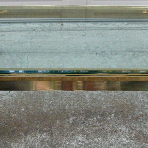 May include: A gold-toned glass coffee table with a rectangular glass top and four curved legs. The table has a polished finish and a modern design.