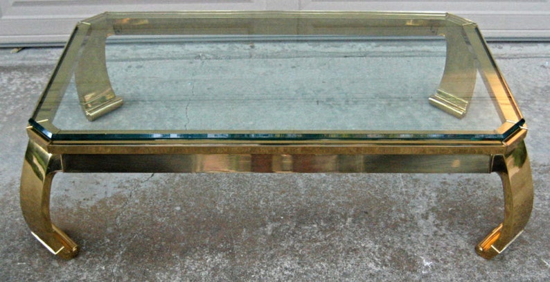 May include: A gold-toned glass coffee table with a rectangular glass top and four curved legs. The table has a polished finish and a modern design.