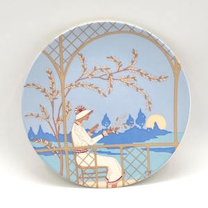 以下が含まれることがあります： 青い白の陶磁器の皿で、庭の風景の中に座っている女性の装飾的なデザインが施されています。女性は白いドレスと帽子を着用しています。庭は格子で囲まれており、背景には木々と花があります。