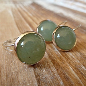 Op de afbeelding: Een set zilveren oorbellen en een ring met groene edelsteen cabochons. De oorbellen hebben een eenvoudig haakontwerp.