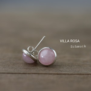 Op de afbeelding: Een paar oorstekers met een lichtroze, ronde steen gezet in een zilverkleurige zetting. De oorbellen worden gepresenteerd op een houten oppervlak. De tekst "VILLA ROSA Schmuck" is zichtbaar.