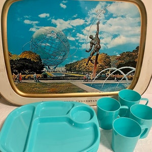 May include: A vintage metal serving tray with a picture of the 1964 New York World's Fair. The tray features a blue and white image of the Unisphere, a statue of a man reaching for the sky, and a fountain. The tray is surrounded by a gold trim. There are also several turquoise plastic plates and cups.